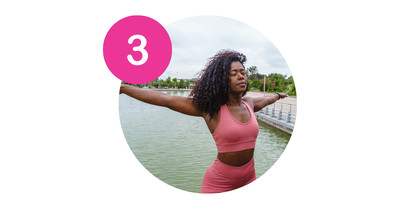 A confident Black woman in athletic wear stretching her arms out by a peaceful lake, representing the feeling of relief and renewed energy after personalized chiropractic care.